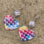 Heart-shaped earrings with colorful heart pattern on a sandy surface