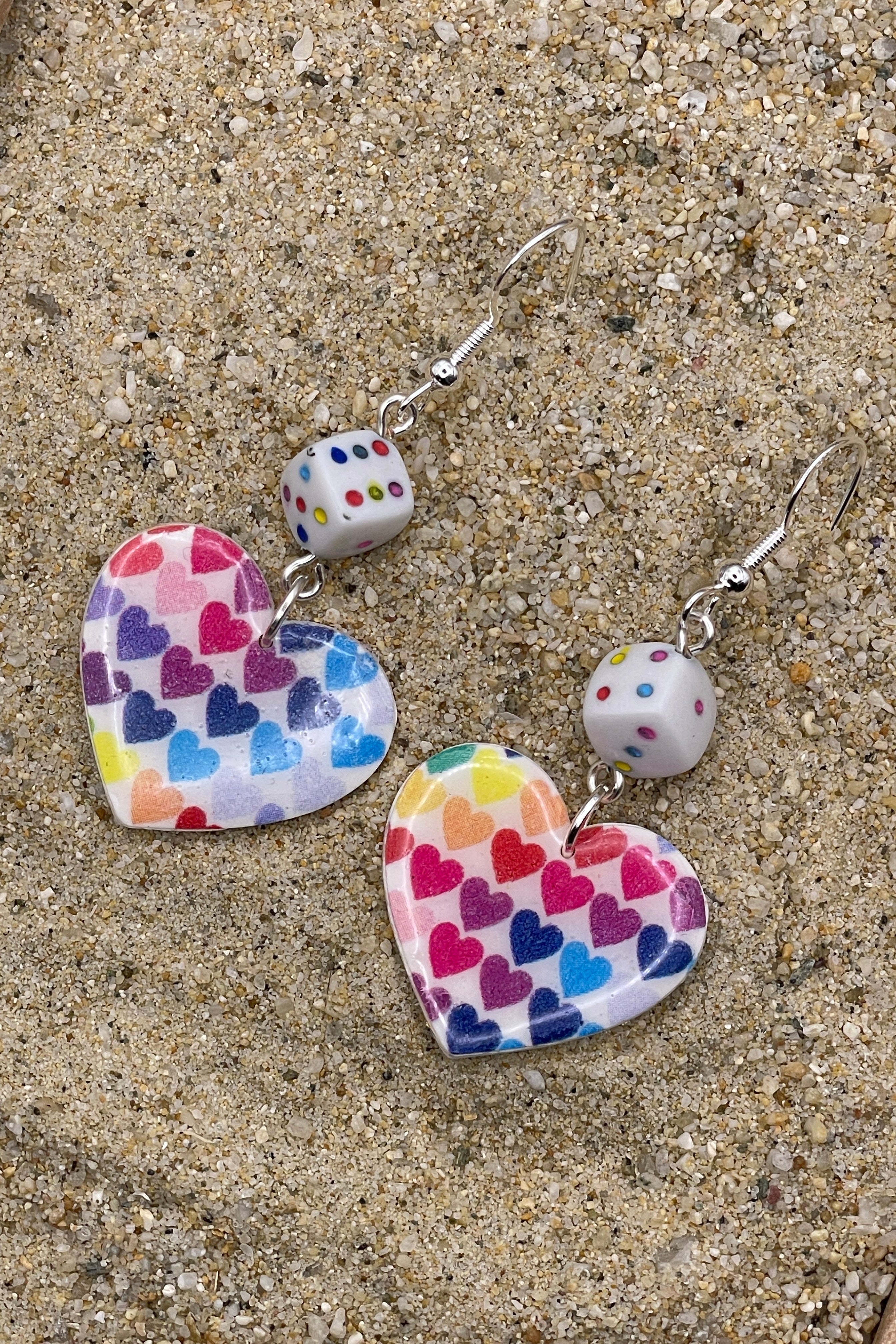 Heart-shaped earrings with colorful heart pattern on a sandy surface