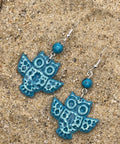 Blue owl-shaped earrings on a sandy surface