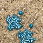 Blue owl-shaped earrings on a sandy surface