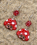 Red and white mushroom-shaped earrings on a textured surface