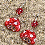 Red and white mushroom-shaped earrings on a textured surface