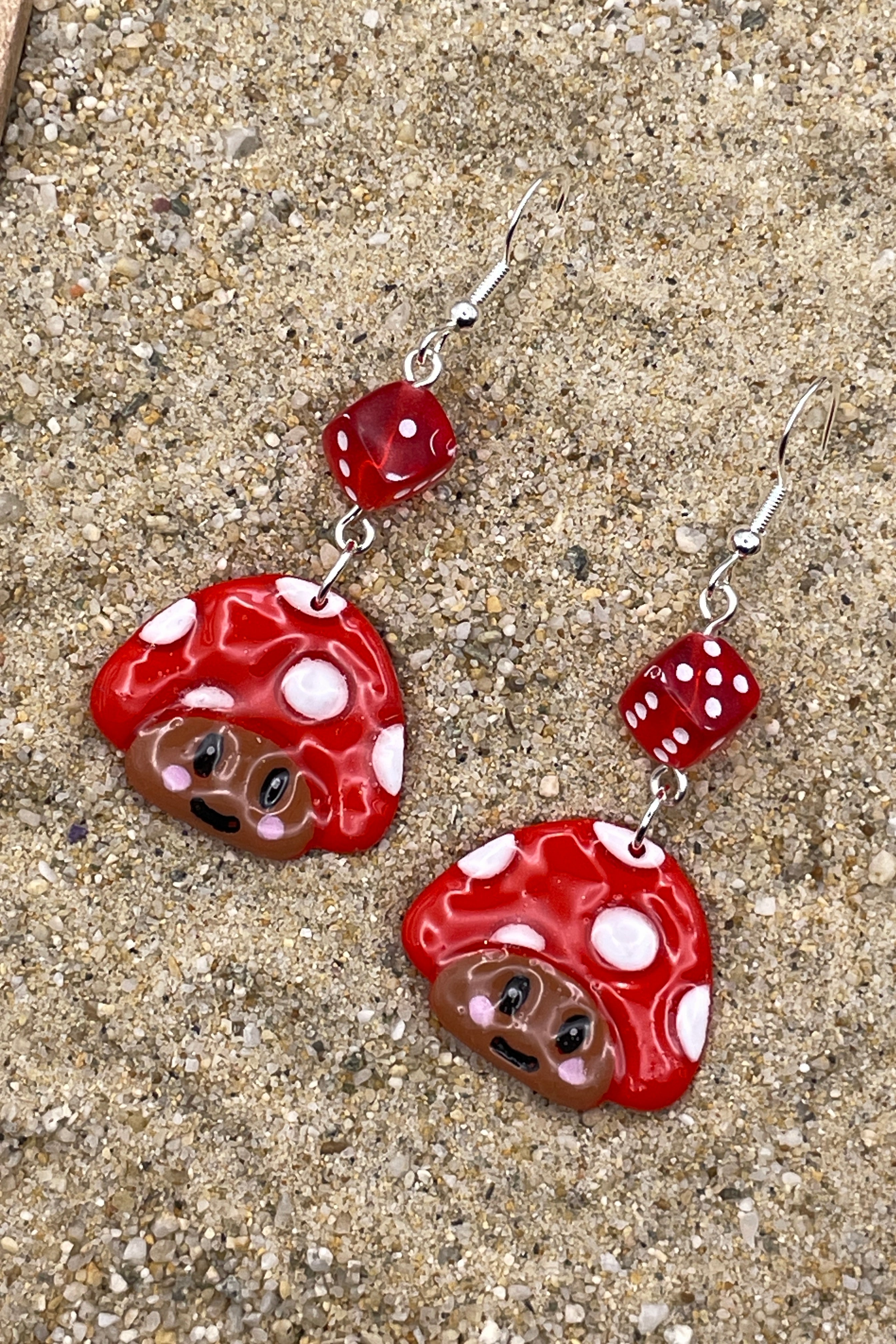 Red and white mushroom-shaped earrings on a textured surface