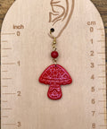 Red mushroom-shaped earring on a wooden gauge with measurements.