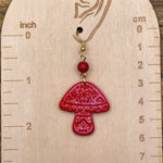 Red mushroom-shaped earring on a wooden gauge with measurements.