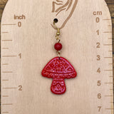 Red mushroom-shaped earring on a wooden gauge with measurements.