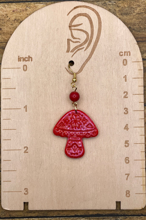 Red mushroom-shaped earring on a wooden gauge with measurements.