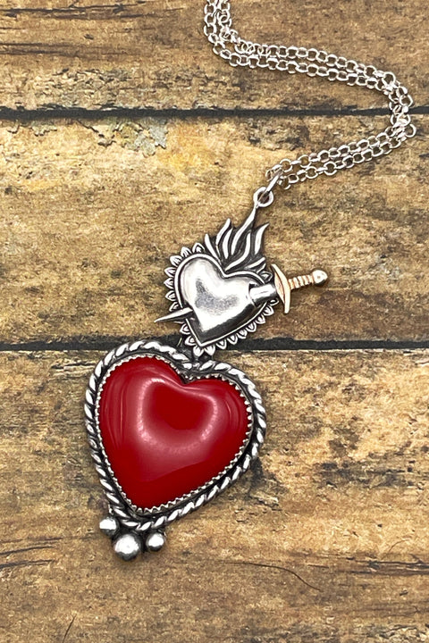 Heart-shaped pendant with a sword on a chain against a wooden background
