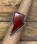 A lightning bolt ring featuring a polished dark red cabochon stone in a silver bezel setting