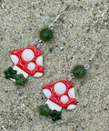Pair of mushroom-shaped earrings on a sandy surface