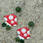 Pair of mushroom-shaped earrings on a sandy surface