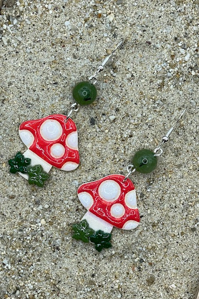 Pair of mushroom-shaped earrings on a sandy surface