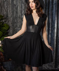 Woman wearing a black dress with a leather corset detail against a textured gray curtain background.