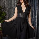 Woman wearing a black dress with a leather corset detail against a textured gray curtain background.
