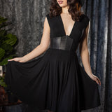 Woman wearing a black dress with a leather corset detail against a textured gray curtain background.