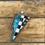 Necklace with a checkered and turquoise lightning bolt shaped pendant on a wooden surface