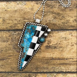 Necklace with a checkered and turquoise lightning bolt shaped pendant on a wooden surface