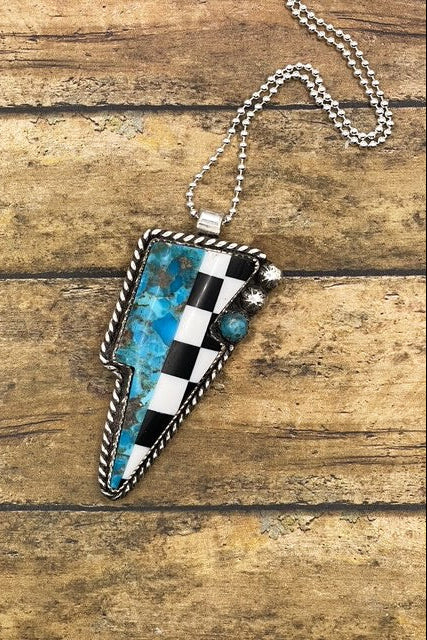 Necklace with a checkered and turquoise lightning bolt shaped pendant on a wooden surface