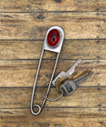 Metal jumbo safety pin key holder with red scorpion design and keys on a wooden surface