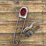 Metal jumbo safety pin key holder with red scorpion design and keys on a wooden surface