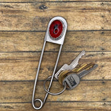 Metal jumbo safety pin key holder with red scorpion design and keys on a wooden surface