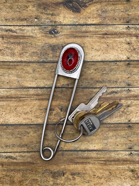 Metal jumbo safety pin key holder with red scorpion design and keys on a wooden surface