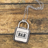 Silver padlock-shaped pendant with 'BAR' on a chain against a wooden background