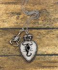 Necklace with a heart-shaped pendant featuring a scorpion design on a wooden surface.