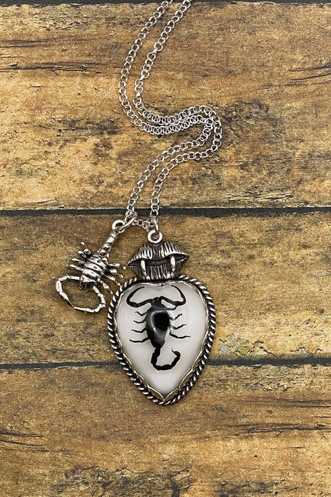 Necklace with a heart-shaped pendant featuring a scorpion design on a wooden surface.