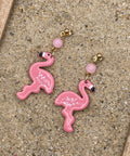 Pink flamingo earrings on a sandy surface