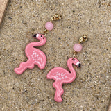 Pink flamingo earrings on a sandy surface