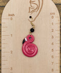 Pink spiral flamingo earring on a wooden measurement chart with inch and cm scales.