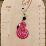 Pink spiral flamingo earring on a wooden measurement chart with inch and cm scales.