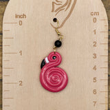 Pink spiral flamingo earring on a wooden measurement chart with inch and cm scales.