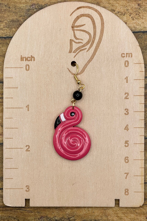 Pink spiral flamingo earring on a wooden measurement chart with inch and cm scales.