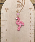 Pink flamingo earring on a wooden gauge with measurements in inches and centimeters.