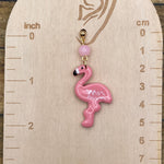 Pink flamingo earring on a wooden gauge with measurements in inches and centimeters.
