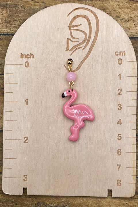 Pink flamingo earring on a wooden gauge with measurements in inches and centimeters.