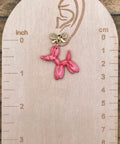 Pink balloon dog earring on a wooden scale against a wooden background