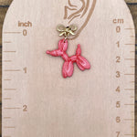 Pink balloon dog earring on a wooden scale against a wooden background