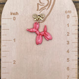 Pink balloon dog earring on a wooden scale against a wooden background