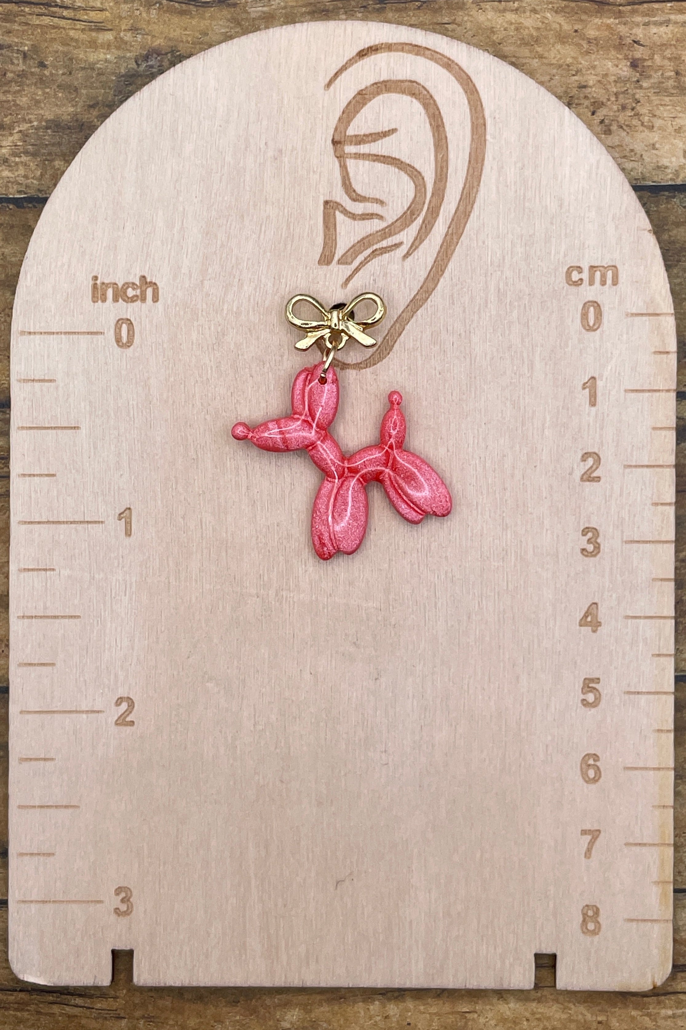 Pink balloon dog earring on a wooden scale against a wooden background