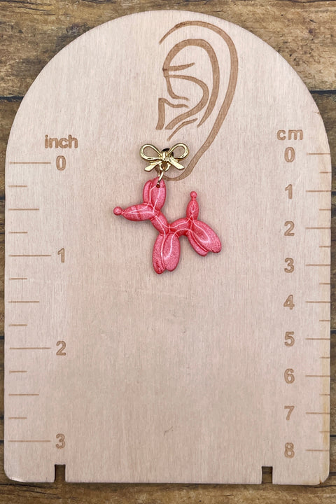 Pink balloon dog earring on a wooden scale against a wooden background