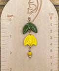 Yellow flower-shaped earring on a wooden measurement card with inch and cm scales.