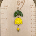 Yellow flower-shaped earring on a wooden measurement card with inch and cm scales.