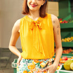 Woman wearing a yellow top and floral skirt with a fruit-themed background