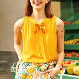 Woman wearing a yellow top and floral skirt with a fruit-themed pattern, standing in front of a produce stand.
