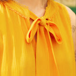 Close-up of a person wearing a yellow sleeveless top with a bow detail.