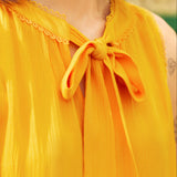 Close-up of a person wearing a yellow sleeveless top with a bow detail.