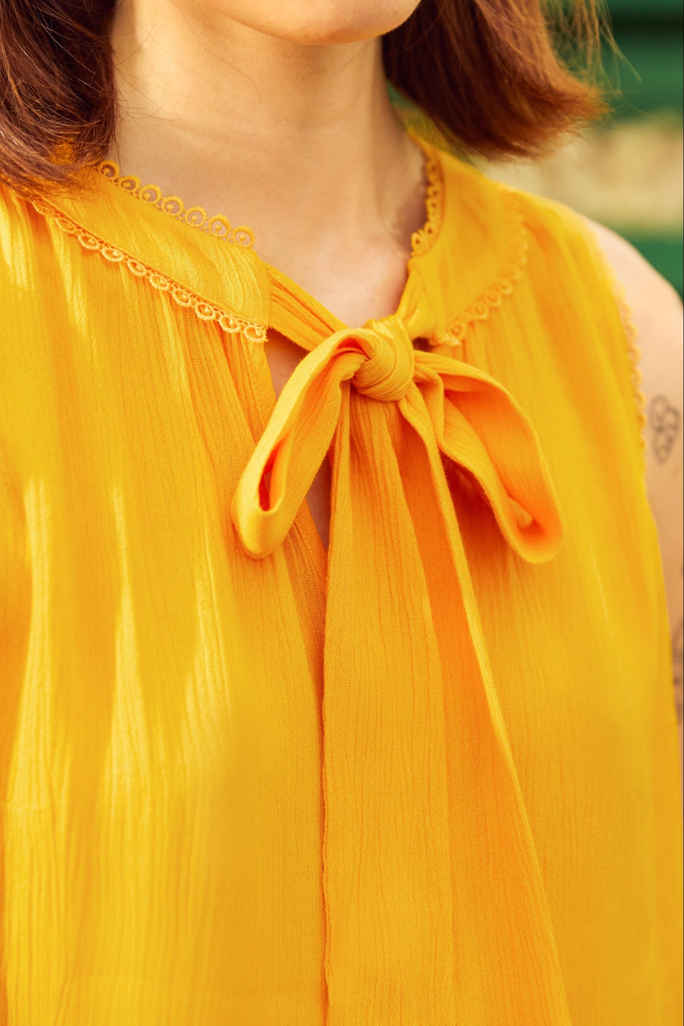 Close-up of a person wearing a yellow sleeveless top with a bow detail.